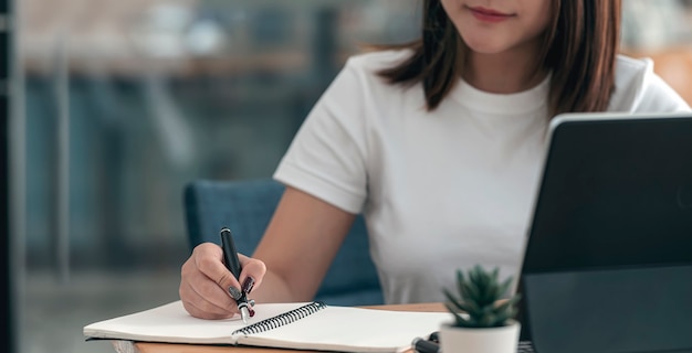 Primo piano imange femminile di scrittura a mano sul taccuino con la penna mentre è seduto alla scrivania in ufficio.