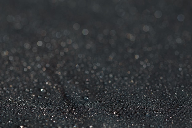 Primo piano in panno piatto idrofobo impermeabile grigio scuro con sfondo di messa a fuoco selettiva di gocce di pioggia