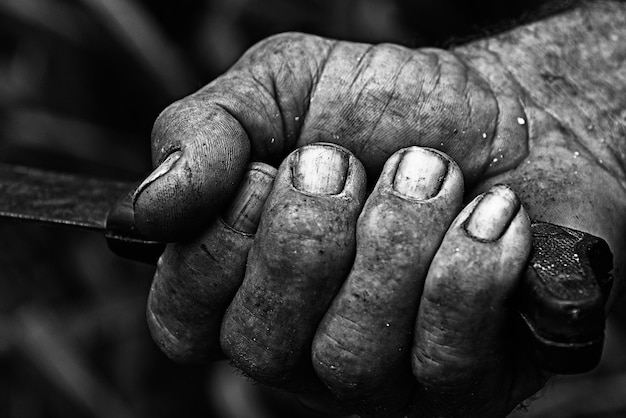 Primo piano in scala di grigi di una mano sporca di un vecchio contadino che afferra una maniglia dello strumento
