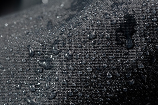 Primo piano in tessuto idrofobico impermeabile grigio scuro con gocce d'acqua sullo sfondo del fuoco selettivo