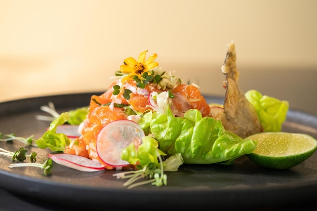 Primo piano Insalata di salmone crudo piccante Stile tailandese decorato con pelle di pesce fritto croccante e fiore giallo in cima e micro erbe intorno al piatto Pronto da servire e mangiare