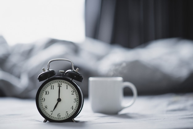 Primo piano - La sveglia ha una buona giornata con una tazza di caffè sulla luce solare del letto di mattina.