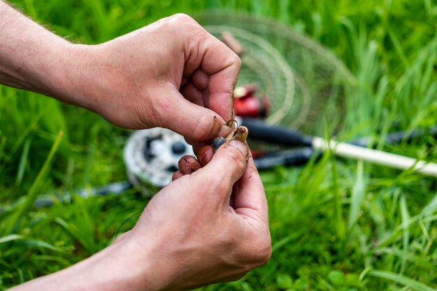 Primo piano Le mani degli uomini mettono l'esca sul gancio per pescare con la canna da pesca Concetto di svago per lo stile di vita Pescatore con verme