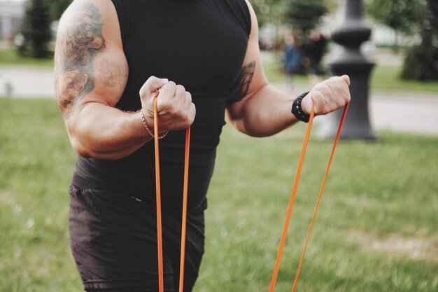 Primo piano mani bell'uomo sportivo che fa allenamento di affondo con fascia di resistenza all'aperto nel parco urbano Concetto di stile di vita sano fitness