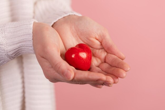 Primo piano mani che tengono il cuore su sfondo rosa concetto di san valentino