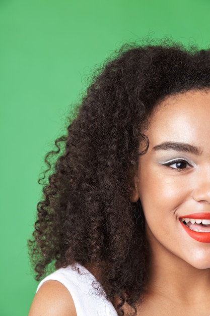 Primo piano mezzo volto ritratto di una bella giovane donna africana che indossa il trucco, guardando lontano isolato su verde