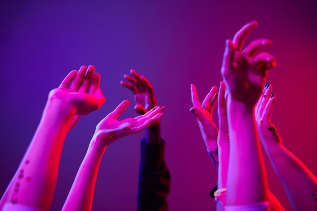 Primo piano minimo di mani in alto alla festa illuminata da luci colorate gruppo di persone che ballano
