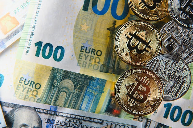 Primo piano mucchio di monete fisiche bitcoin dorate sopra il fuoco selettivo della vista ad alto angolo dello sfondo delle banconote in dollari in euro