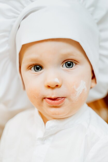 Primo piano piccolo ragazzo sporco caucasico curioso divertente in un cappello da cuoco esamina la macchina fotografica