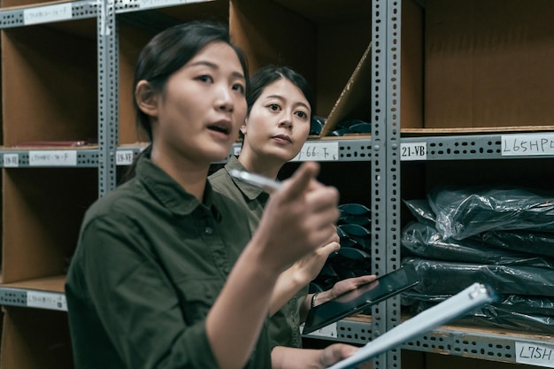 primo piano ragazza lavoratore che mostra qualcosa al collega in magazzino. gruppo di dipendenti giapponesi asiatici che camminano nel magazzino controllando i prodotti di stoccaggio. colleghe che lavorano in magazzino.