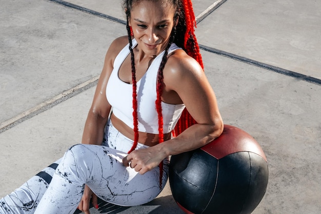 Primo piano Riposo Donna atletica che fa esercizio con palla medica Forza e motivazioneFoto di donna sportiva in abbigliamento sportivo alla moda