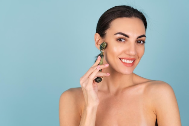 Primo piano ritratto di bellezza di una donna con pelle perfetta e trucco naturale, labbra carnose nude, con in mano un massaggiatore a rullo per viso e collo