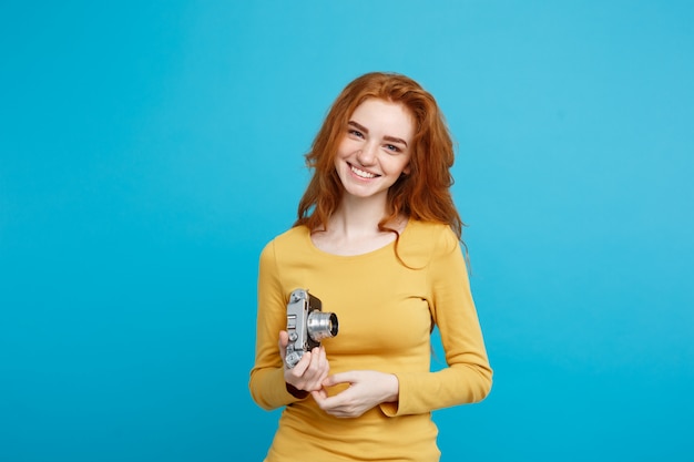 Primo piano Ritratto di giovane bella ragazza attraente zenzero felice sorridente con la fotocamera d&#39;epoca e pronto a viaggiare. Isolato su sfondo blu pastello. Copia spazio.