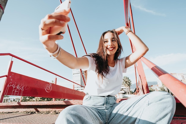 Primo piano ritratto di giovane donna araba che prende una camicia bianca selfie e jeans blu in una strada. sfrontatezza. Stile di vita di strada, cool trendy. Concetto di rete sociale. Colpo grandangolare