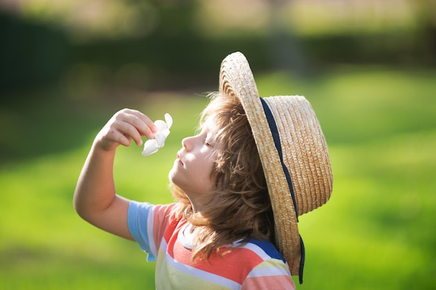 Primo piano ritratto di un simpatico bambino con cappello di paglia che odora di fiori di plumeria. Infanzia e concetto di genitorialità. Vacanze estive.