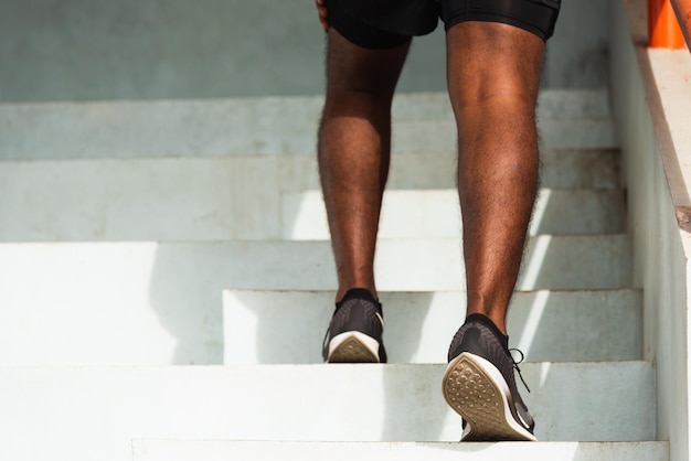 Primo piano scarpe da atleta di gambe giovane corridore sportivo uomo nero passo che corre fino a salire le scale facendo allenamento allenamento cardio sport sulla strada all'aperto, sano esercizio prima del concetto di allenamento