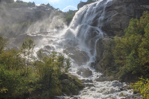 Primo piano scene cascata in montagna, parco nazionale Dombai, Caucaso, Russia, Europa. Paesaggio estivo, tempo soleggiato, cielo azzurro drammatico e giornata di sole