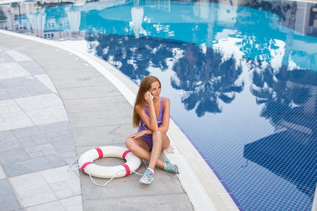 Primo piano selfieritratto di una ragazza attraente con i capelli lunghi in piedi vicino alla piscina Sorride alla telecamera e mostra un look accattivante Cappello di paglia sulla testa In vacanza in resort
