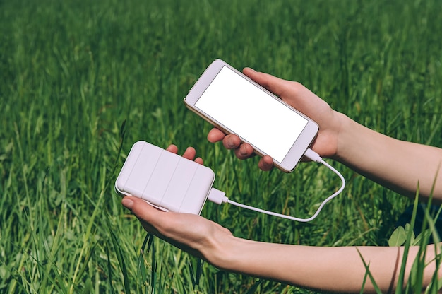 Primo piano sul telefono cellulare in bianco con power bank tenuto in mano