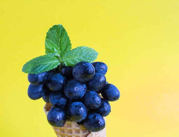 Primo piano sull'uva blu nel cono gelato sullo sfondo giallo. Copia spazio.
