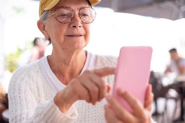 Primo piano sulla donna anziana con cappello e occhiali usando il telefono mentre è seduto al tavolo di un bar Donna caucasica dipendente seduta al tavolo del ristorante godendo di tecnologia e social