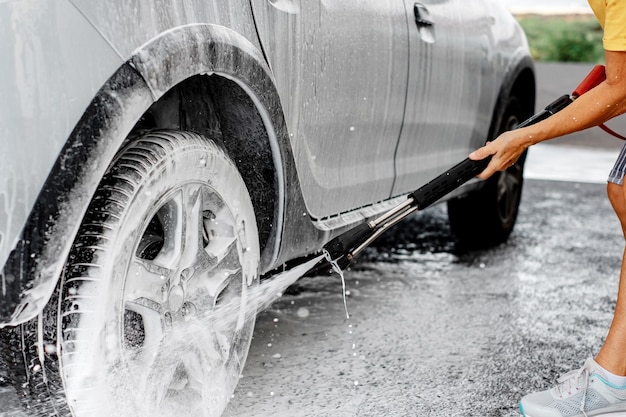 Primo piano sulla donna che tiene la pompa ad alta pressione che lava la sua auto in una stazione di lavaggio auto self-service utilizzando acqua ad alta pressione Autolavaggio self-service