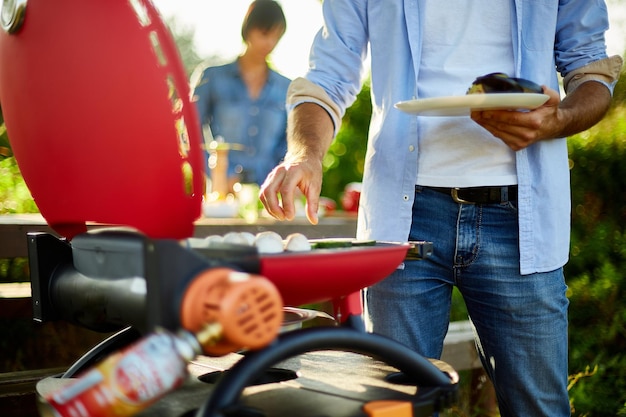 Primo piano sulla mano dell'uomo che arrostisce le verdure sulla griglia a gas del barbecue