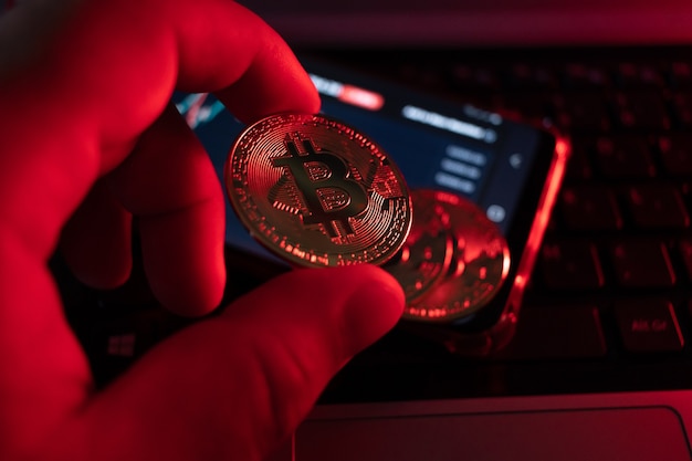 Primo piano sulla moneta bitcoin con illuminazione rossa che allude alla caduta della moneta, profondità di campo molto ridotta.