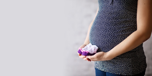 Primo piano sulla pancia incinta. Donna che aspetta un bambino con una pancia che tiene i calzini del bambino