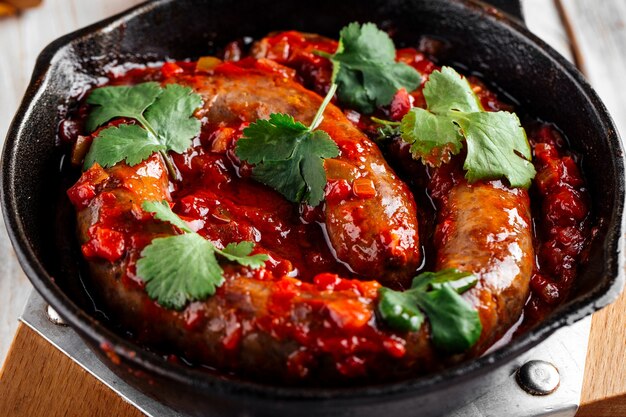 Primo piano sulla salsiccia grande cotta in salsa di pomodoro in padella di ghisa