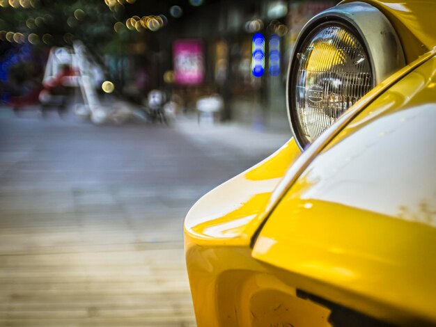 Primo piano sulla vecchia auto gialla vintage, luce anteriore sopra lo spazio pubblico con luce bokeh