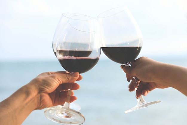 Primo piano sulle mani che tengono bicchieri di vino rosso sulla spiaggia, concetto di celebrazione