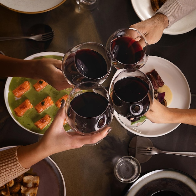 Primo piano sulle mani che tostano vino rosso su piatti fusion - vista dall'alto piatto di amici che tintinnano bicchieri di vino