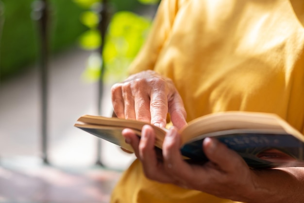 Primo piano sulle mani della donna anziana in camicia gialla che riposa nel parco pubblico leggendo un libro donna caucasica che si gode la pensione e il tempo libero