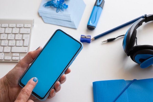 Primo piano sulle mani della donna che tengono lo smartphone con display blu. Colore blu sugli accessori