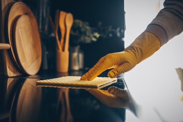 Primo piano sulle mani della donna in guanti di gomma protettivi gialli che puliscono i mobili della cucina con la spugna