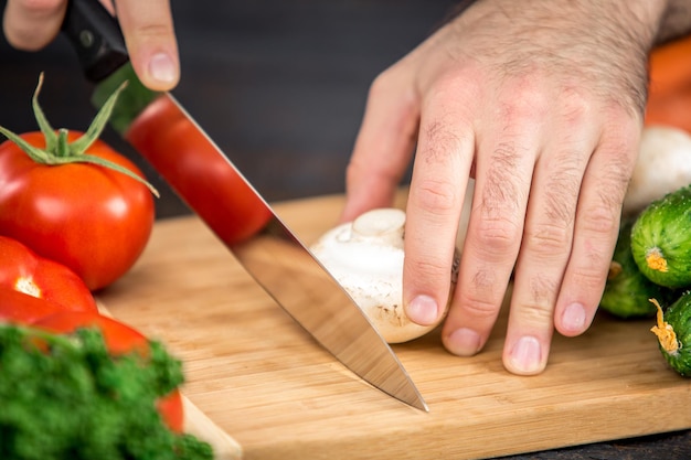 Primo piano sulle mani maschili che tagliano il pomodoro, facendo l'insalata. Capo taglio verdure. Stile di vita sano, cibo dietetico