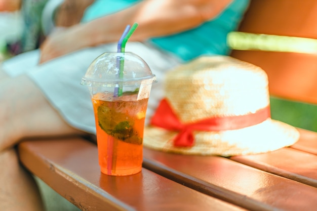 Primo piano tazza di plastica da asporto con cocktail aperol spritz su panca di legno nel giardino mattutino