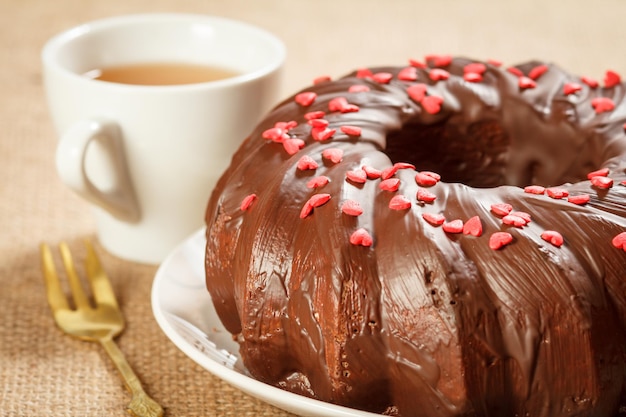 Primo piano torta al cioccolato fatta in casa decorata con piccoli cuori di caramello sul piatto e tazza di tè sul tavolo. Profondità di campo.