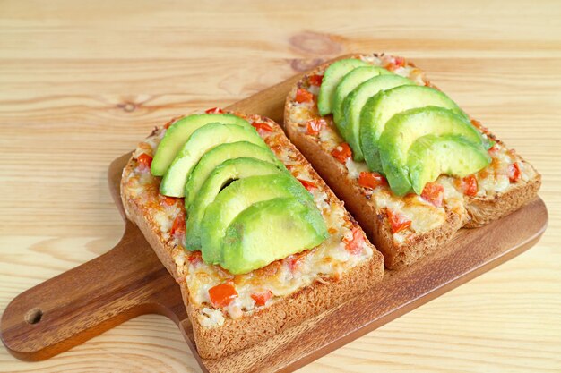 Primo piano un paio di toast fatti in casa con formaggio grigliato conditi con avocado e pomodoro su breadboard