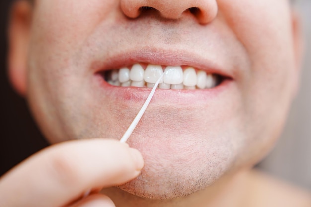 Primo piano un uomo lavarsi i denti stuzzicadenti di plastica con filo interdentale