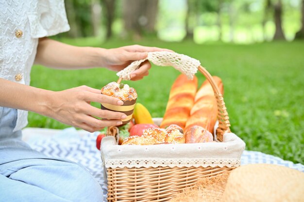 Primo piano Una femmina si siede su una coperta da picnic e tiene in mano un cesto di vimini di dolci da dessert