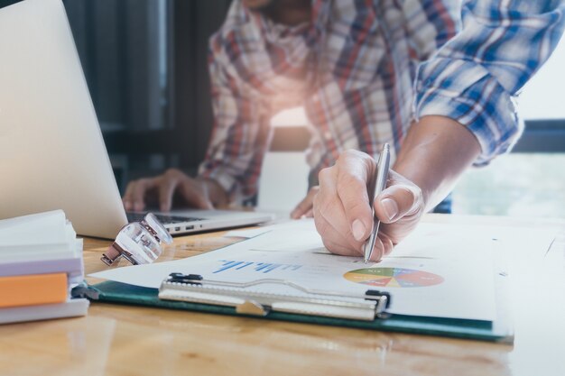 Primo piano Uomini d&#39;affari mani a lavorare con piano finanziario e su scrivania in legno in ufficio. Concetto di sostegno del gruppo.