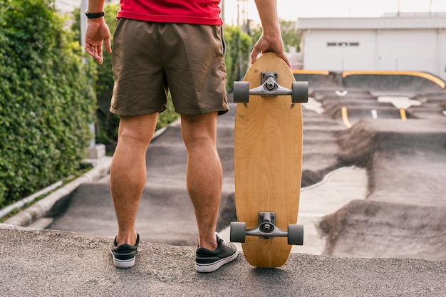 Primo piano uomo asiatico che tiene surfskate o skateboard in pumptrack skate Park