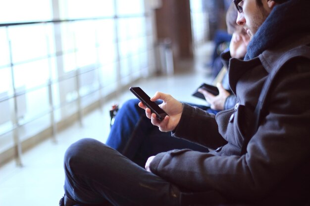 Primo piano uomo moderno con smartphone seduto nell'edificio dell'aeroporto