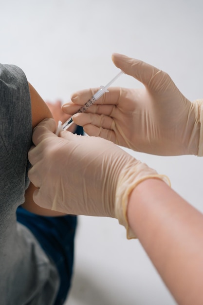 Primo piano verticale del medico che effettua la dose di iniezione di vaccinazione covid19 nella spalla Primo piano delle mani dell'infermiere che vaccina il maschio