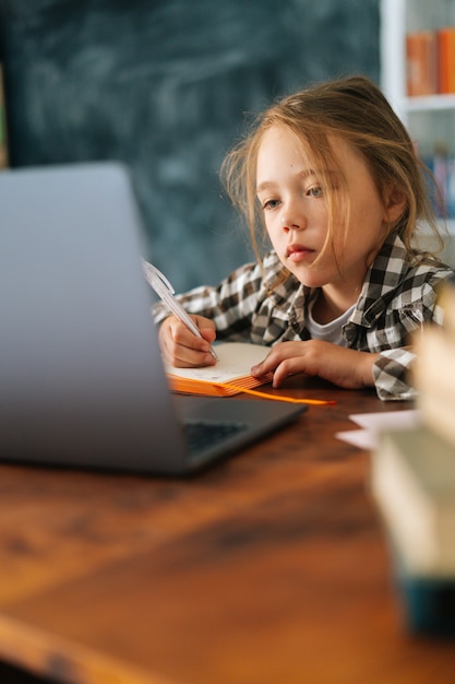 Primo piano verticale di una studentessa carina e focalizzata che fa i compiti a casa scrivendo note con la penna