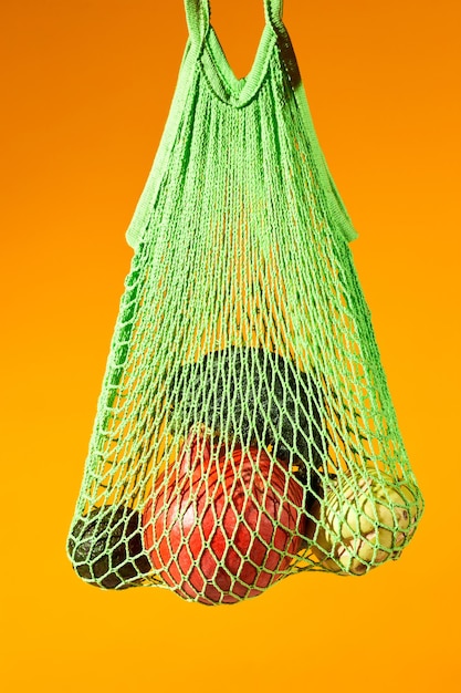 Primo piano verticale di verdure fresche in eco net bag su sfondo arancione vibrante consumo consapevole