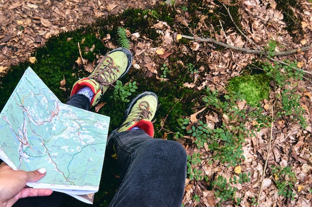 Primo piano viaggiatore utilizzando la mappa locale. Vista dall'alto di scarpone da trekking sul sentiero. Legs In Jeans E scarpe da trekking sportive sulle pietre rocciose delle montagne. Viaggio locale.