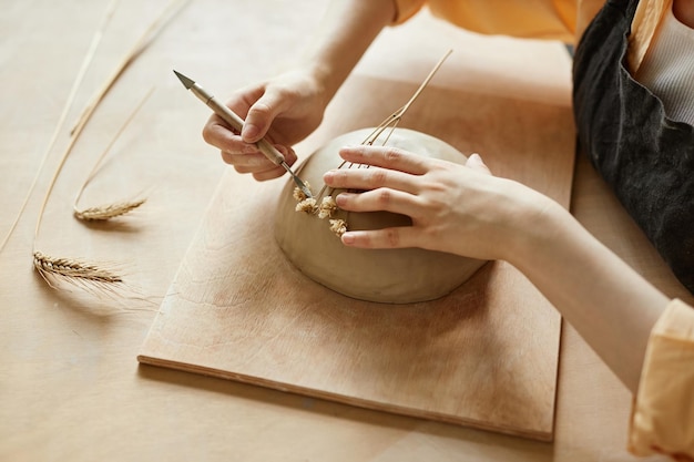 Primo piano vista dall'alto di artigiane femminili che decorano ceramiche fatte a mano con impronta vegetale utilizzando immortelle